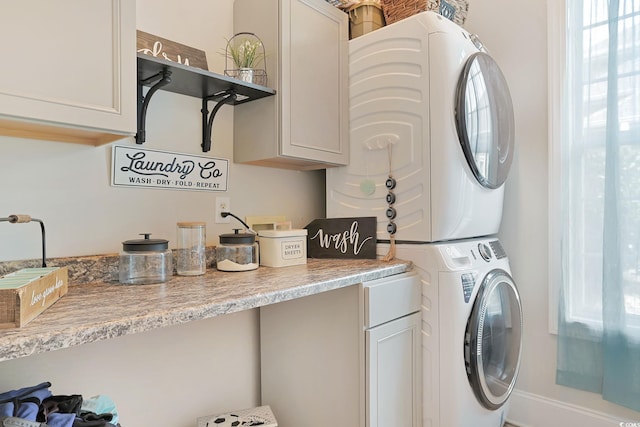 clothes washing area with stacked washer / drying machine and cabinets