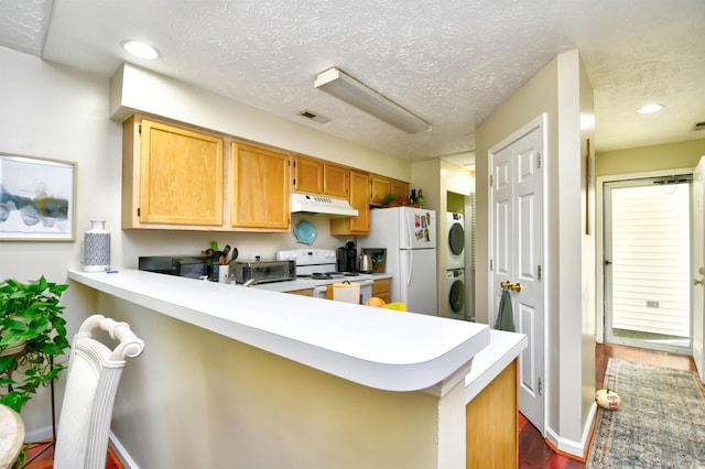 kitchen featuring stacked washer / drying machine, kitchen peninsula, a textured ceiling, and white appliances