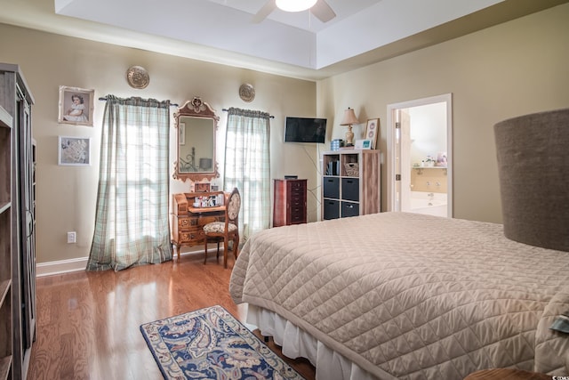 bedroom featuring a raised ceiling, hardwood / wood-style flooring, ceiling fan, and ensuite bathroom