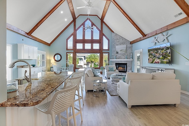 living room featuring a fireplace, light wood-type flooring, beam ceiling, high vaulted ceiling, and sink