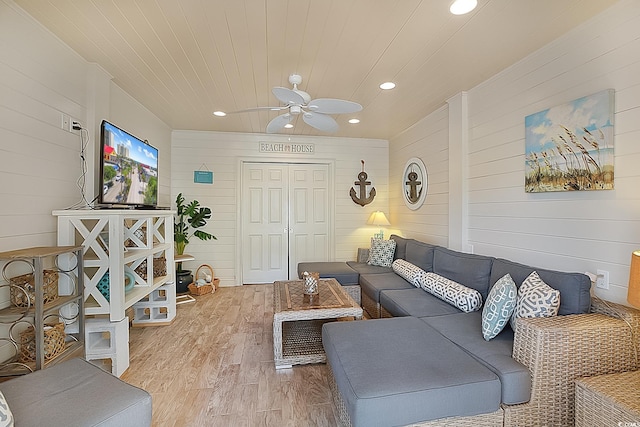 living room featuring ceiling fan, wood-type flooring, and wooden walls