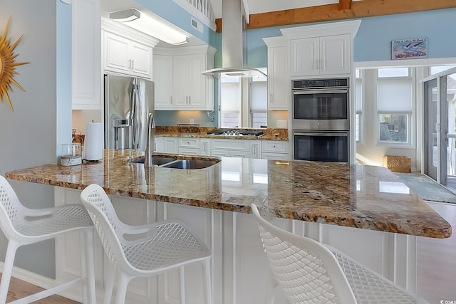 kitchen with stone countertops, white cabinetry, sink, appliances with stainless steel finishes, and island range hood