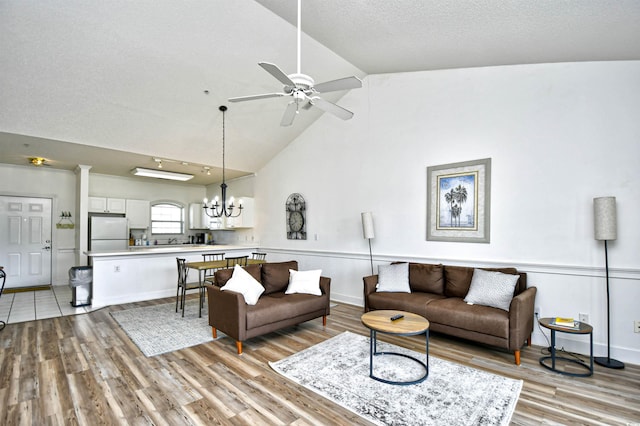 living room with ceiling fan with notable chandelier, a textured ceiling, light wood-type flooring, and high vaulted ceiling