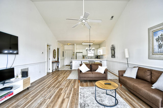 living room with high vaulted ceiling, light hardwood / wood-style flooring, and ceiling fan with notable chandelier