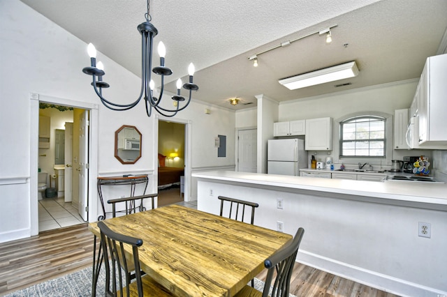 dining space featuring wood-type flooring, a notable chandelier, a textured ceiling, sink, and ornamental molding