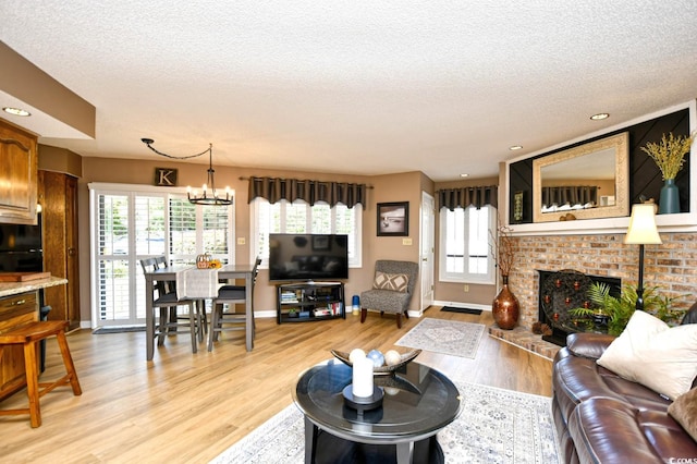 living room featuring a brick fireplace, light hardwood / wood-style flooring, a notable chandelier, and a textured ceiling