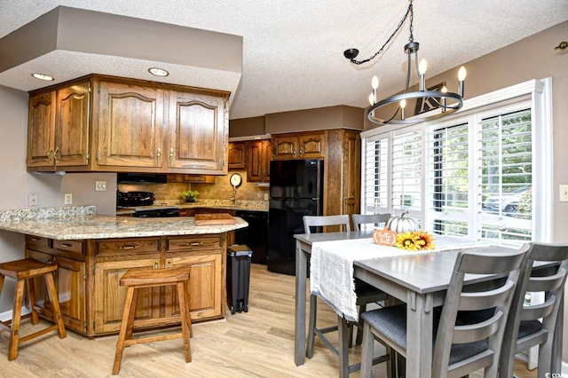 kitchen with light hardwood / wood-style floors, a textured ceiling, black appliances, and light stone counters