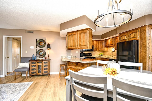 kitchen with black appliances, decorative light fixtures, a textured ceiling, sink, and light hardwood / wood-style flooring