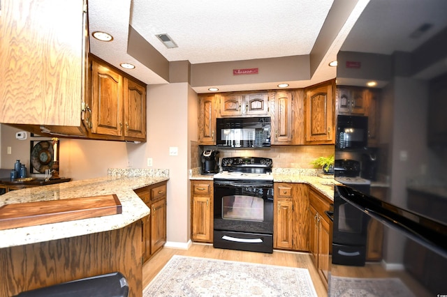 kitchen with light hardwood / wood-style floors, black appliances, tasteful backsplash, light stone countertops, and a textured ceiling