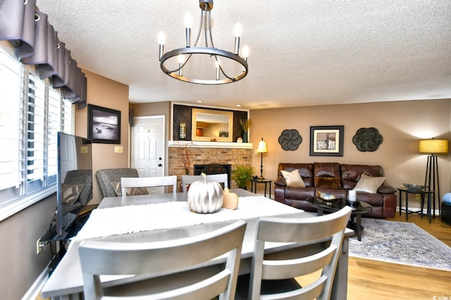 dining space with a chandelier, a textured ceiling, hardwood / wood-style flooring, and a fireplace