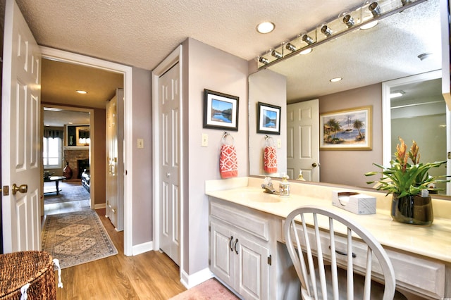 bathroom with a stone fireplace, hardwood / wood-style floors, vanity, and a textured ceiling