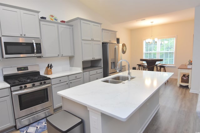 kitchen featuring a center island with sink, stainless steel appliances, light wood-type flooring, sink, and vaulted ceiling