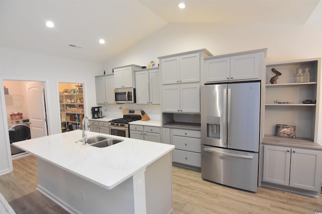 kitchen featuring stainless steel appliances, vaulted ceiling, sink, an island with sink, and washer / clothes dryer