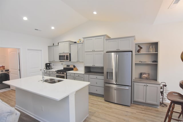 kitchen with stainless steel appliances, vaulted ceiling, sink, light hardwood / wood-style flooring, and washer / clothes dryer