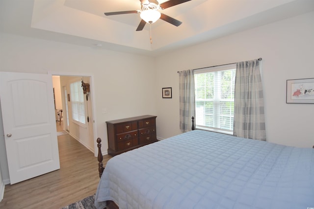 bedroom featuring light hardwood / wood-style floors, ceiling fan, and a raised ceiling