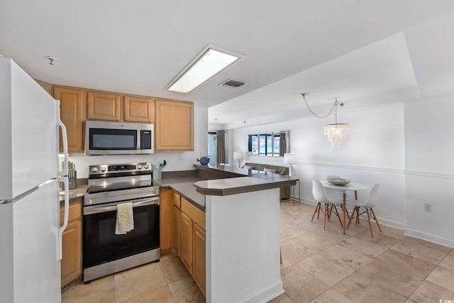 kitchen featuring kitchen peninsula, pendant lighting, appliances with stainless steel finishes, and a notable chandelier