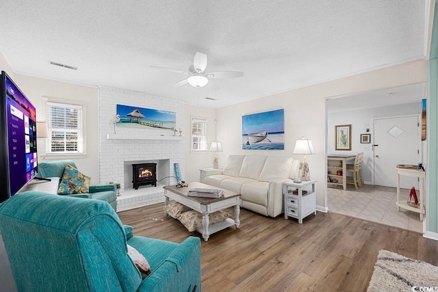 living room with hardwood / wood-style flooring, ceiling fan, a textured ceiling, and a wood stove