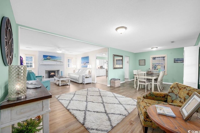 living room featuring a brick fireplace, light hardwood / wood-style flooring, and ceiling fan