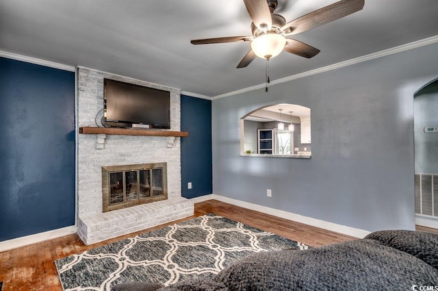 living room featuring a fireplace, ceiling fan, crown molding, and wood-type flooring