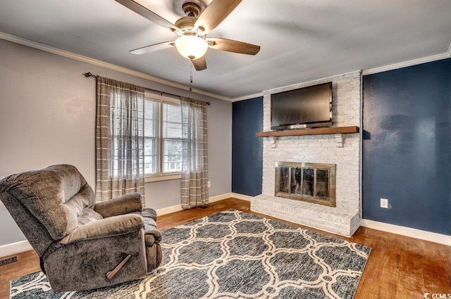 living room with ceiling fan, wood-type flooring, ornamental molding, and a brick fireplace