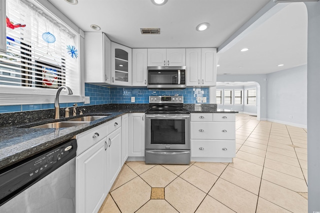 kitchen featuring sink, tasteful backsplash, dark stone counters, white cabinets, and appliances with stainless steel finishes