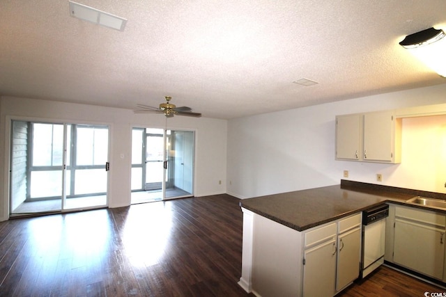 kitchen with dark wood-type flooring, kitchen peninsula, a textured ceiling, and white dishwasher