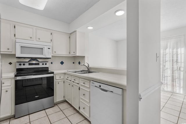 kitchen featuring tasteful backsplash, light tile patterned floors, sink, white cabinets, and white appliances