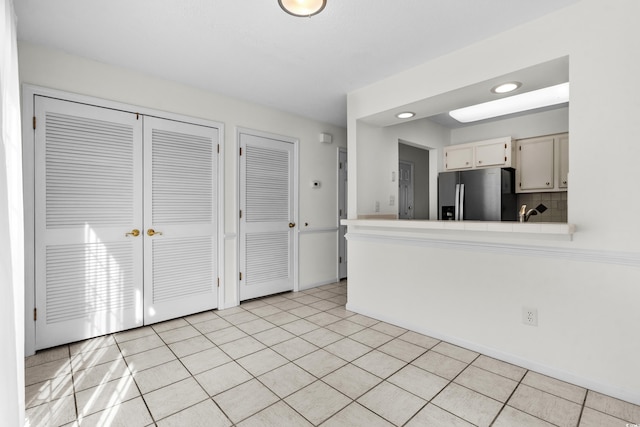 kitchen featuring backsplash, stainless steel refrigerator with ice dispenser, light tile patterned flooring, and white cabinets