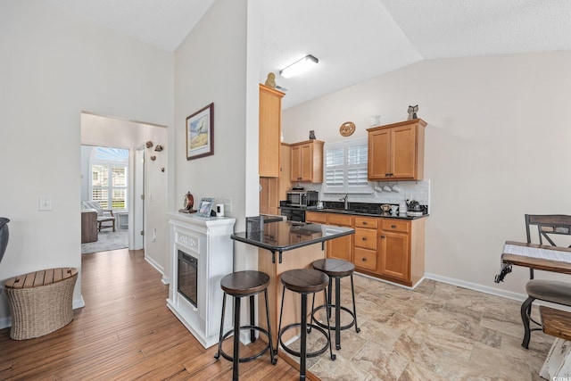 kitchen featuring lofted ceiling, a kitchen bar, sink, dark stone countertops, and backsplash