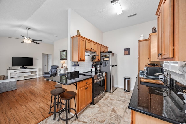 kitchen featuring lofted ceiling, a textured ceiling, dark stone countertops, appliances with stainless steel finishes, and ceiling fan