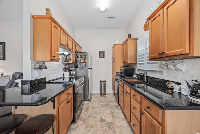 kitchen featuring sink, a breakfast bar area, appliances with stainless steel finishes, dark stone counters, and decorative backsplash