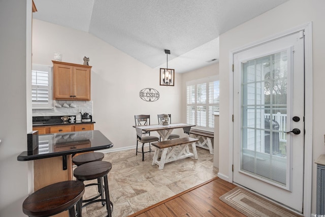 dining room featuring vaulted ceiling, a chandelier, a textured ceiling, and light hardwood / wood-style floors