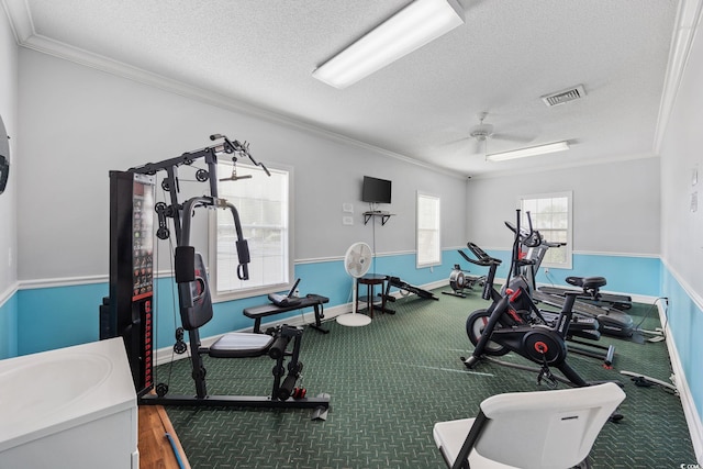 exercise room featuring crown molding, ceiling fan, and a textured ceiling