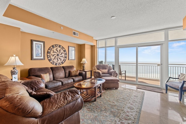 tiled living room featuring a textured ceiling, a water view, and floor to ceiling windows