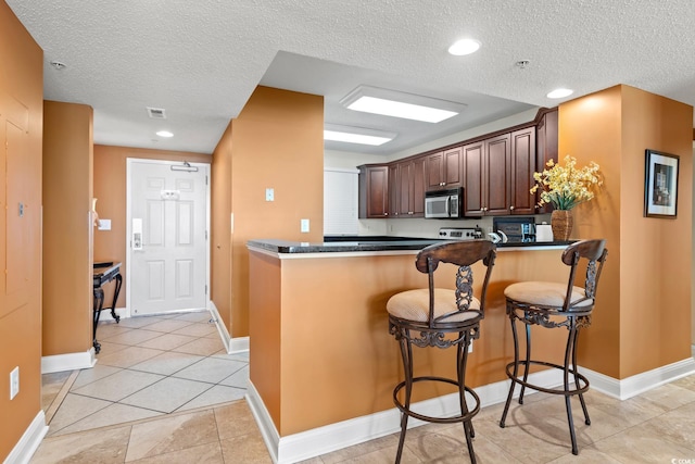 2709 Ocean Blvd S Unit 1202, Myrtle Beach, SC 29577 - kitchen with stainless steel microwave, a textured ceiling, dark countertops, a peninsula, and a kitchen breakfast bar