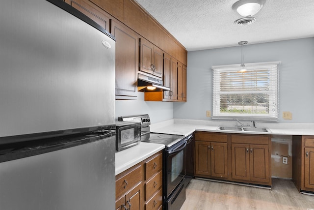 kitchen featuring light wood-type flooring, black electric range oven, sink, pendant lighting, and stainless steel refrigerator