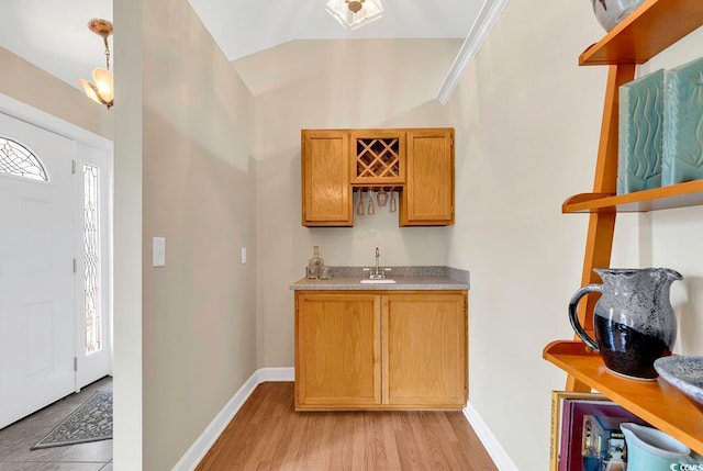 bar featuring light hardwood / wood-style floors, sink, pendant lighting, and lofted ceiling