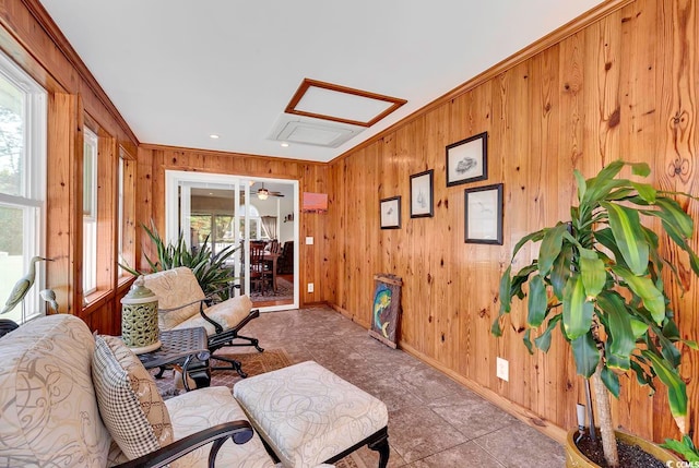 living area featuring light tile patterned flooring, ceiling fan, wooden walls, and crown molding