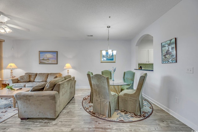 dining area with a textured ceiling, light hardwood / wood-style flooring, and ceiling fan with notable chandelier