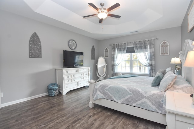 bedroom with a tray ceiling, dark wood-type flooring, and ceiling fan