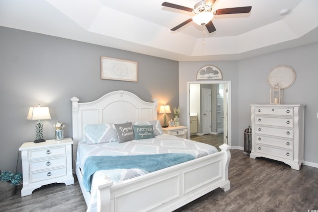 bedroom with ensuite bathroom, dark wood-type flooring, ceiling fan, and a tray ceiling