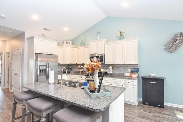 kitchen with sink, a breakfast bar area, an island with sink, stainless steel appliances, and backsplash