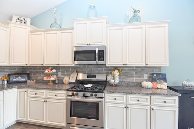 kitchen with lofted ceiling, dark stone counters, backsplash, stainless steel appliances, and white cabinets