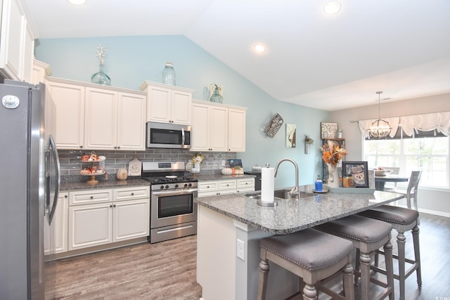 kitchen with decorative light fixtures, lofted ceiling, sink, stainless steel appliances, and a center island with sink