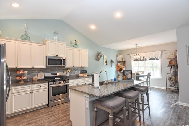 kitchen featuring vaulted ceiling, appliances with stainless steel finishes, pendant lighting, an island with sink, and sink