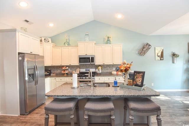 kitchen with a breakfast bar, sink, vaulted ceiling, stainless steel appliances, and a kitchen island with sink