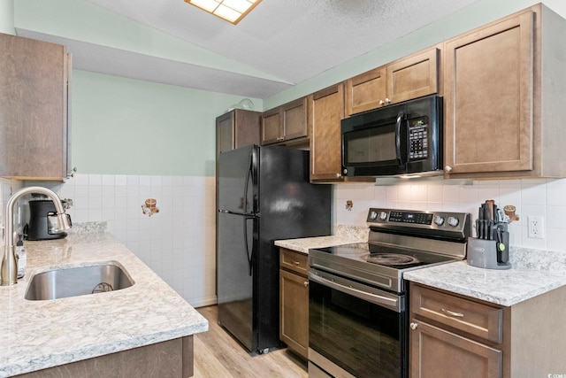 8546 Hopkins Cir Unit G, Surfside Beach, SC 29575 - kitchen featuring black appliances, a sink, lofted ceiling, light wood-type flooring, and tile walls