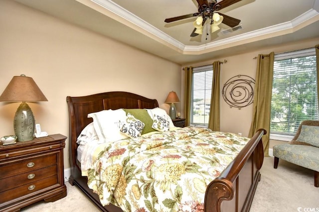 carpeted bedroom featuring ornamental molding, ceiling fan, multiple windows, and a tray ceiling