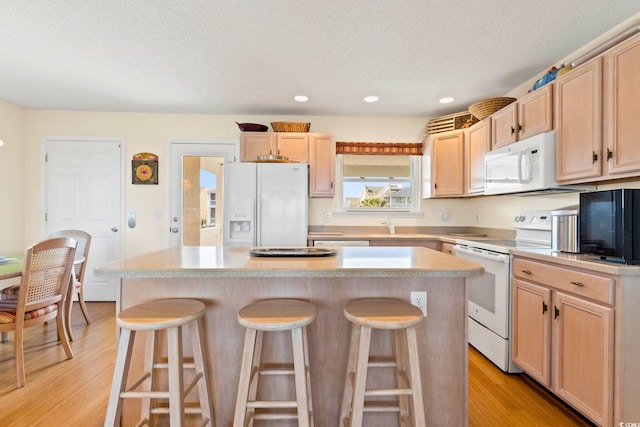 kitchen featuring a kitchen island, white appliances, a kitchen bar, and light hardwood / wood-style flooring