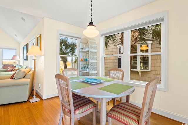 dining area with light wood-type flooring and vaulted ceiling